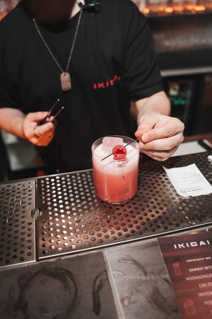 Bartender garnishing a pink cocktail with tweezers